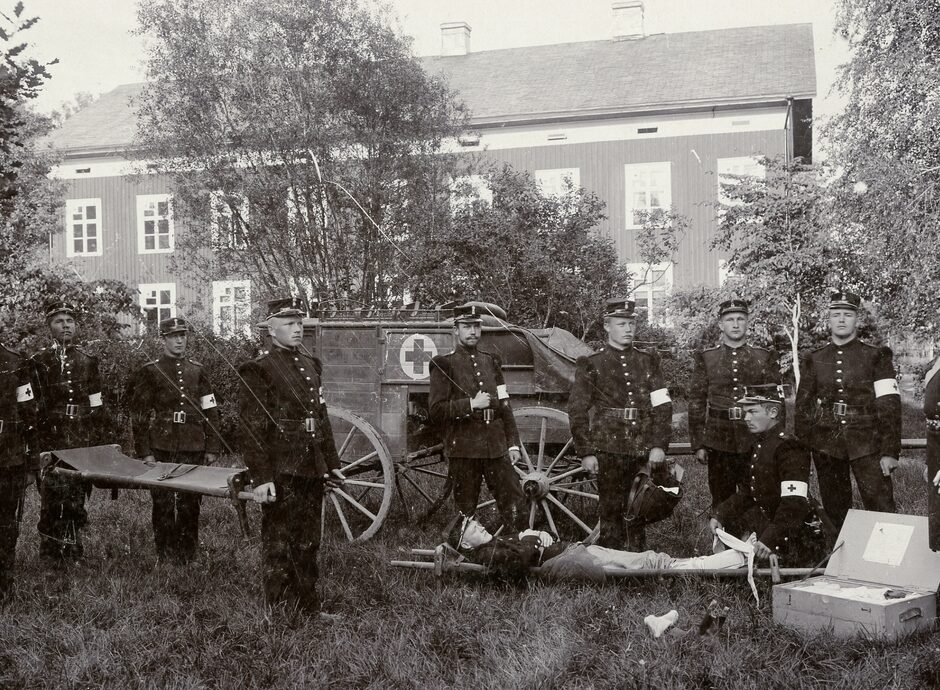 Män i uniformer uppställda bredvid en sjukvagn, en bår och andra sjukvårdsattiraljer.