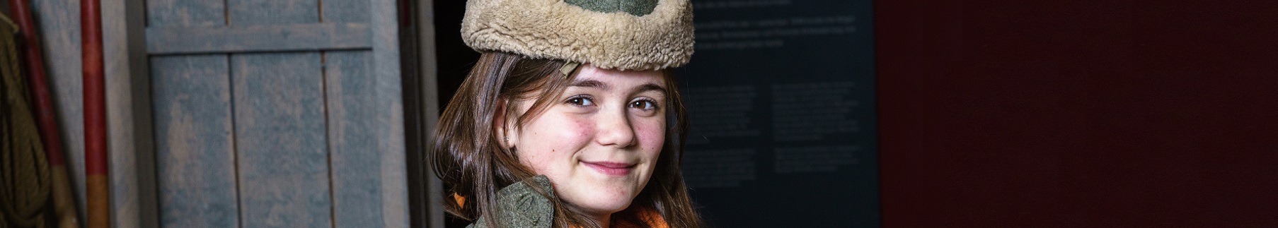 Ett barn tittar in i kameran iförd rock och pälsmössa.