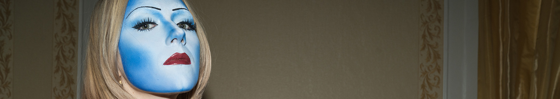 En kvinna med ansiktet helt målat i ljusblått, som en mask.