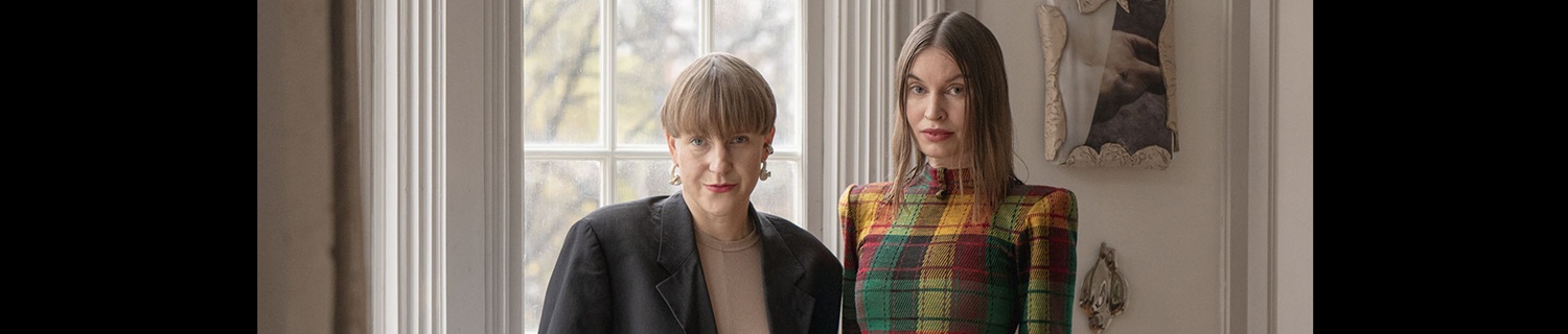 Två personer står vid ett burspråk, tittar in i kameran.