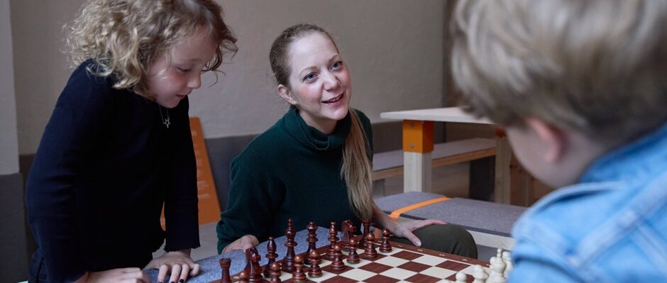 Tv&aring; barn och en vuxen som spelar schack i museimilj&ouml;.